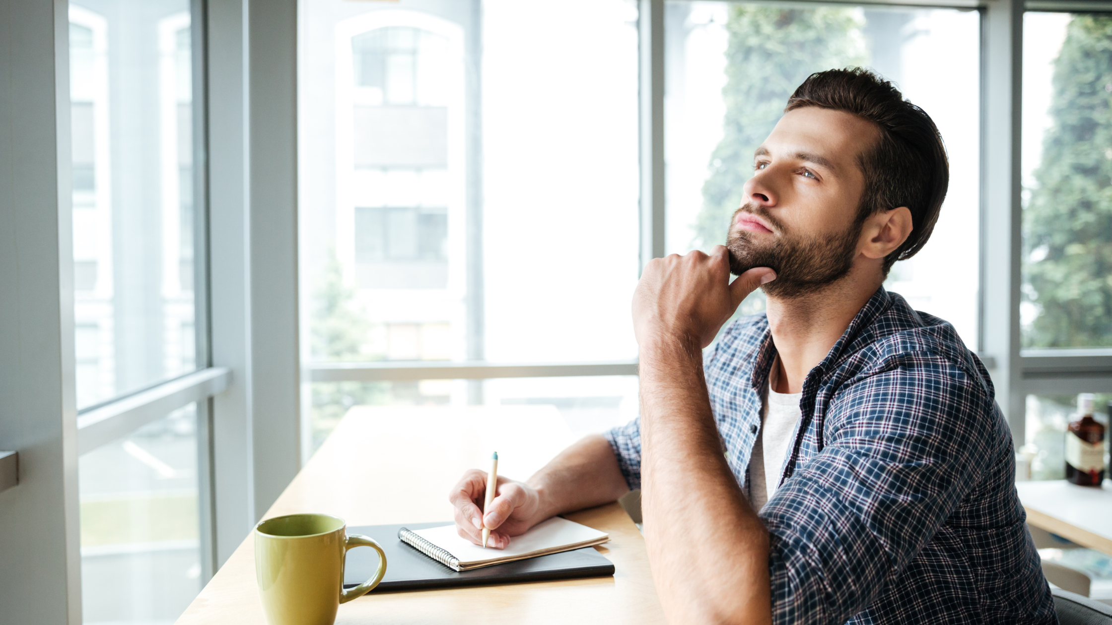 man sitting at the table with a notepad and pen, thinking