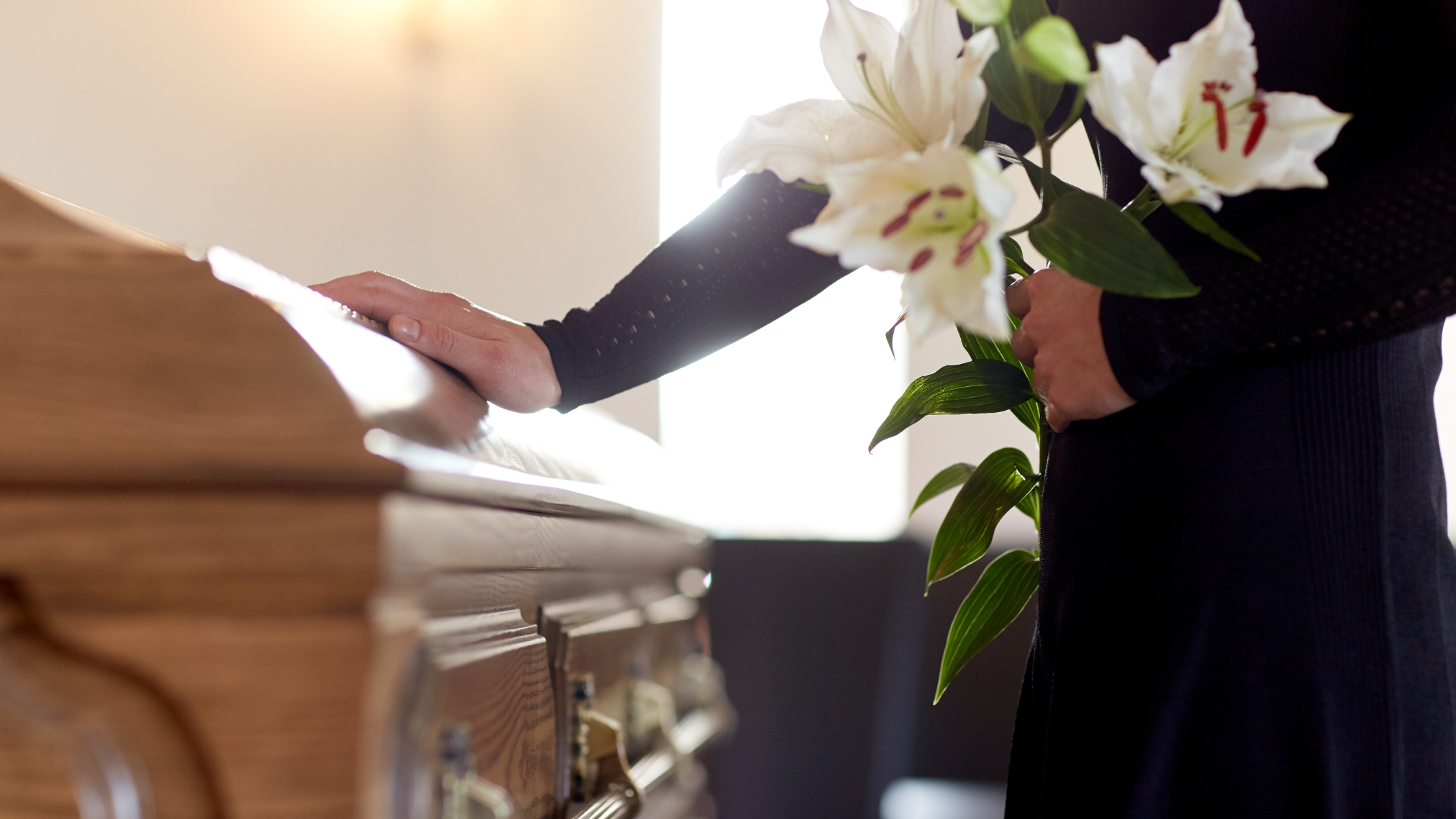 Person holding flowers and touching the casket of their loved one